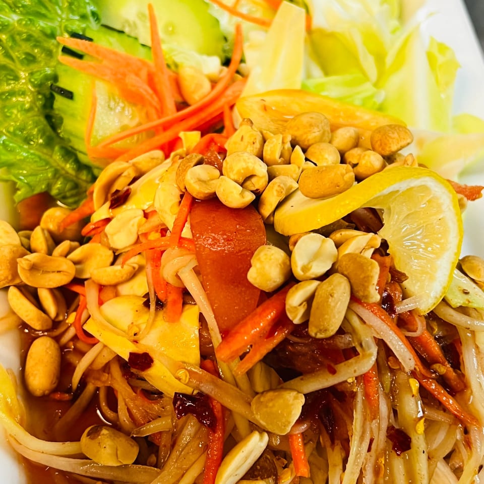 Spicy papaya salad topped with peanuts, carrots, and lemon with fresh vegetables.