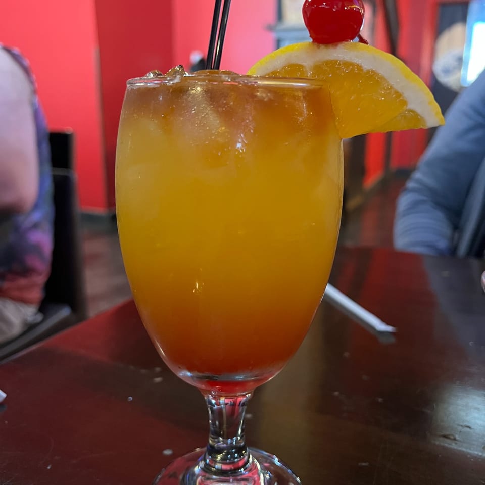 Tropical orange cocktail garnished with an orange slice and cherry.