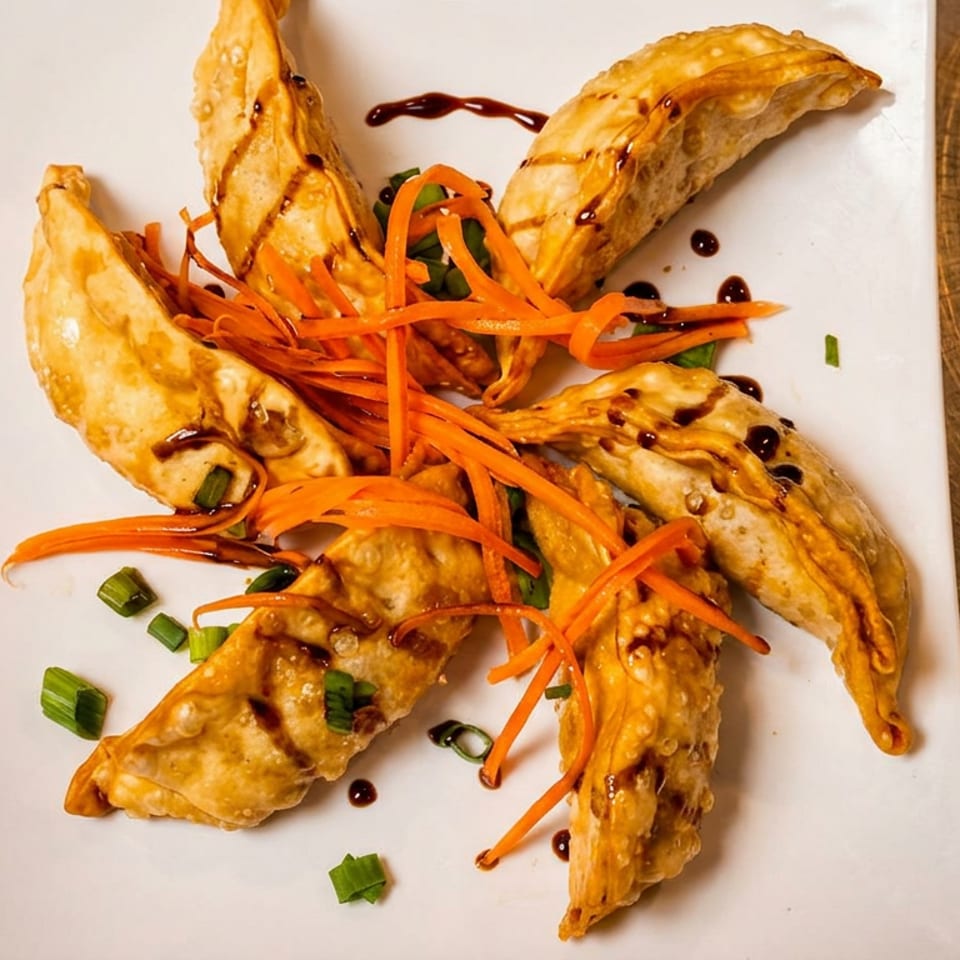 Crispy dumplings topped with shredded carrots, scallions, and dark sauce on a white plate.